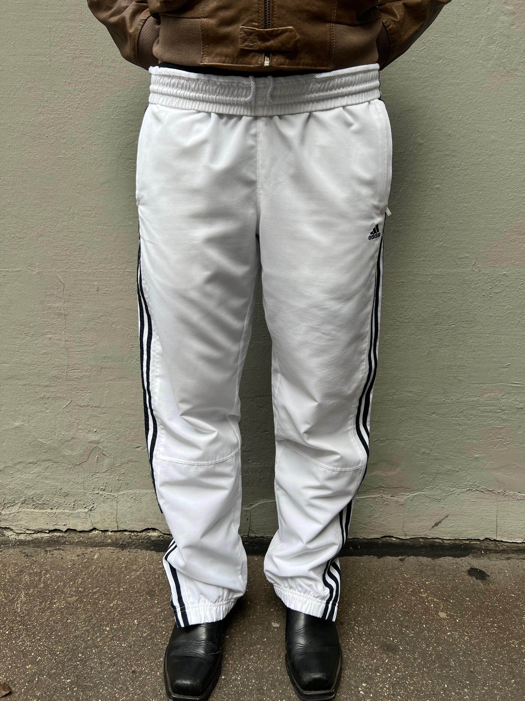 Zu sehen ist eine weiße Adidas Trackpants mit schwarzen Streifen an der Seite 