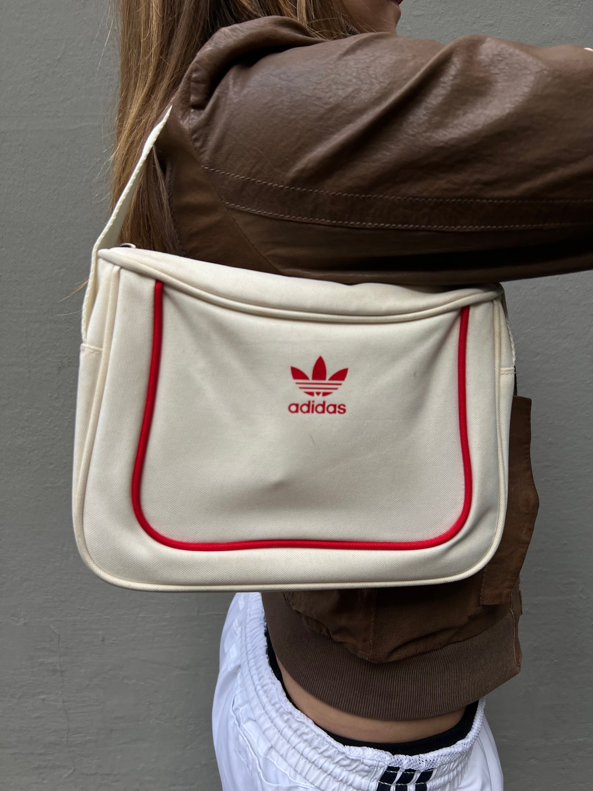 Zu sehen ist eine kleine rechteckige Adidas Tasche in weiß mit roten Details