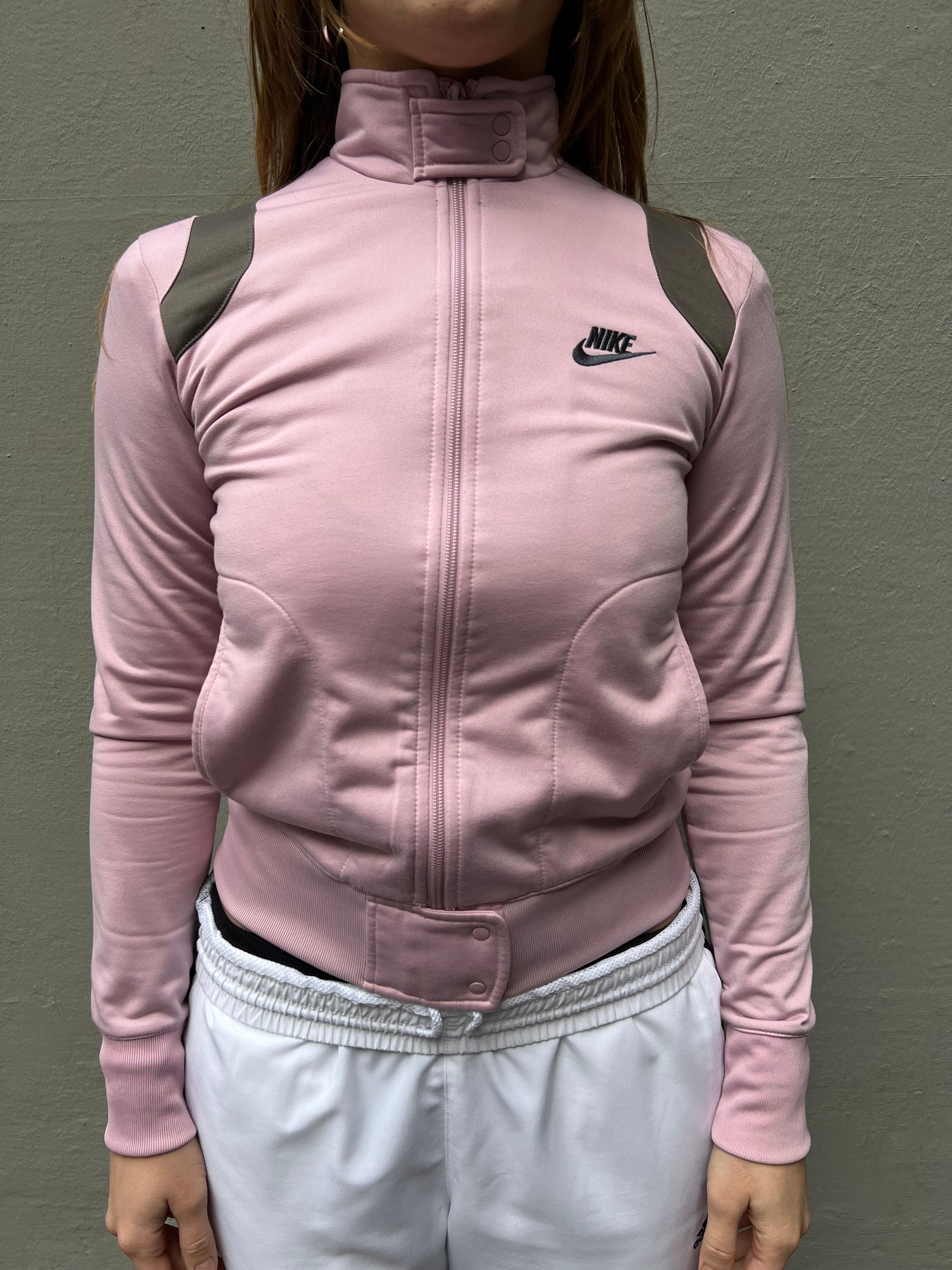 Zu sehen ist eine rosa Nike Trackjacke mit hohem Kragen und braunen Details 