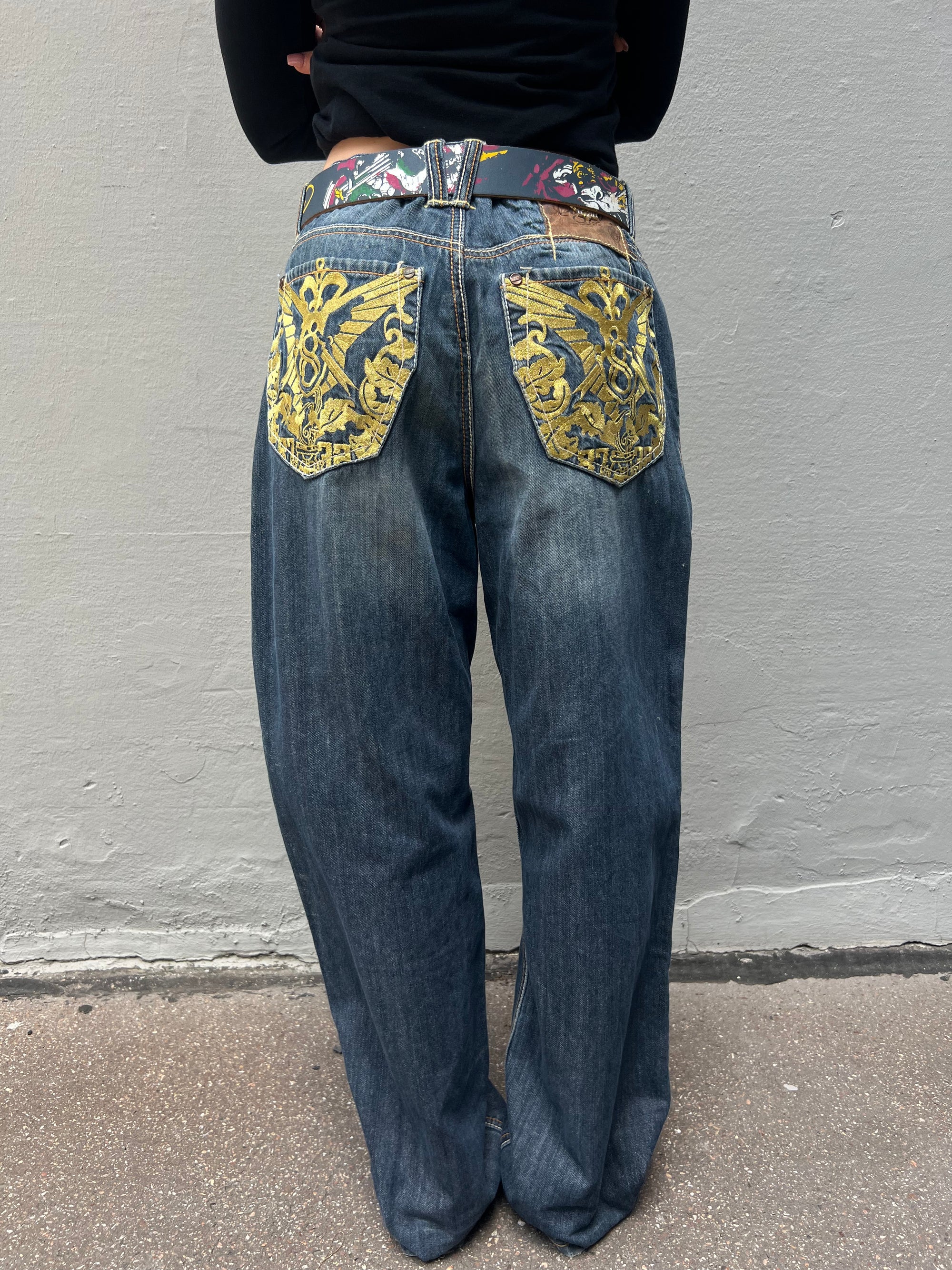 Zu sehen ist eine Vintage Baggy Ed Hardy Jeans getragen vor einem grauen Hintergrund
