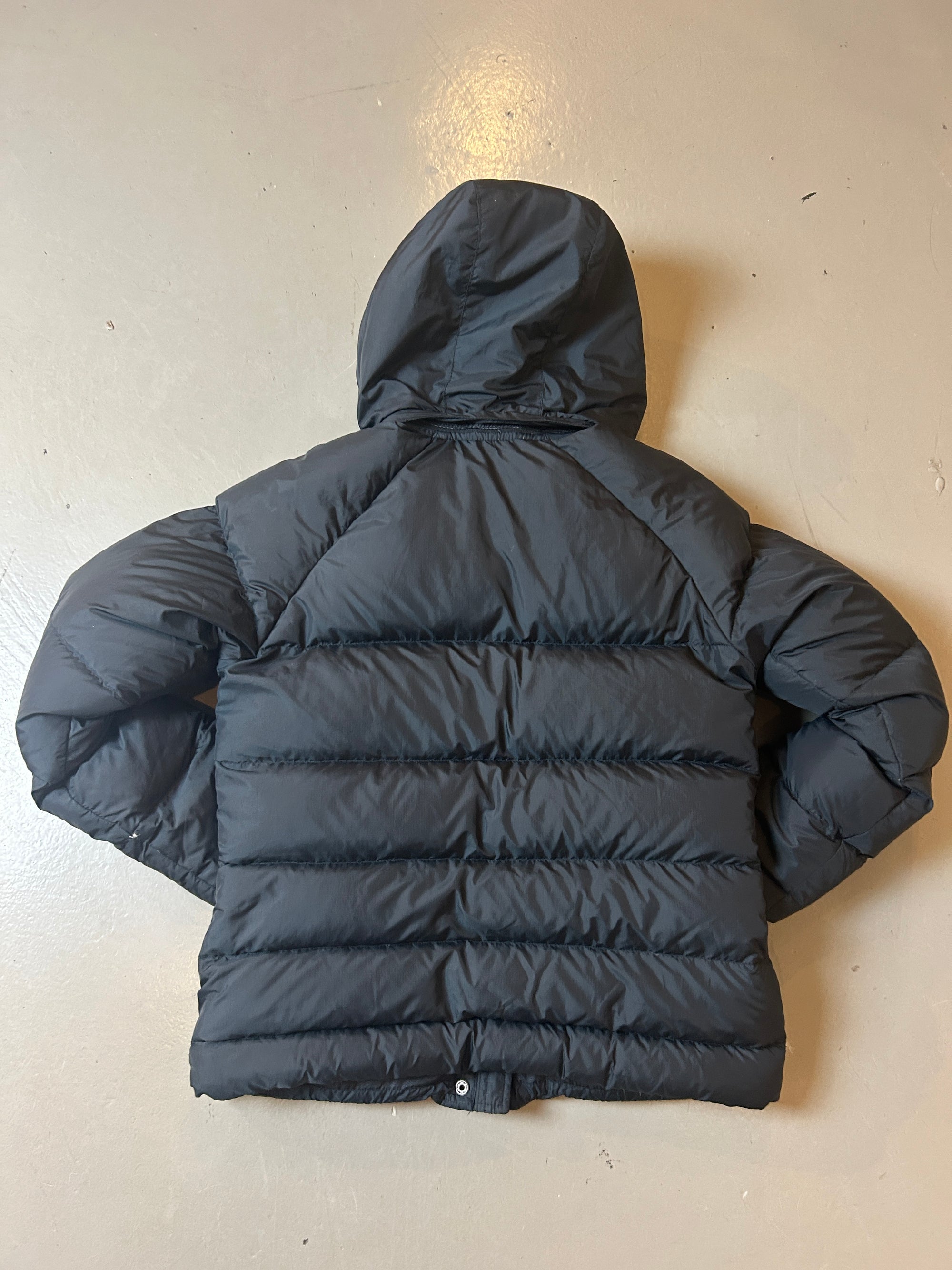 Produktbild von Pufferjacke mit Kapuze von hinten auf grauem Boden 