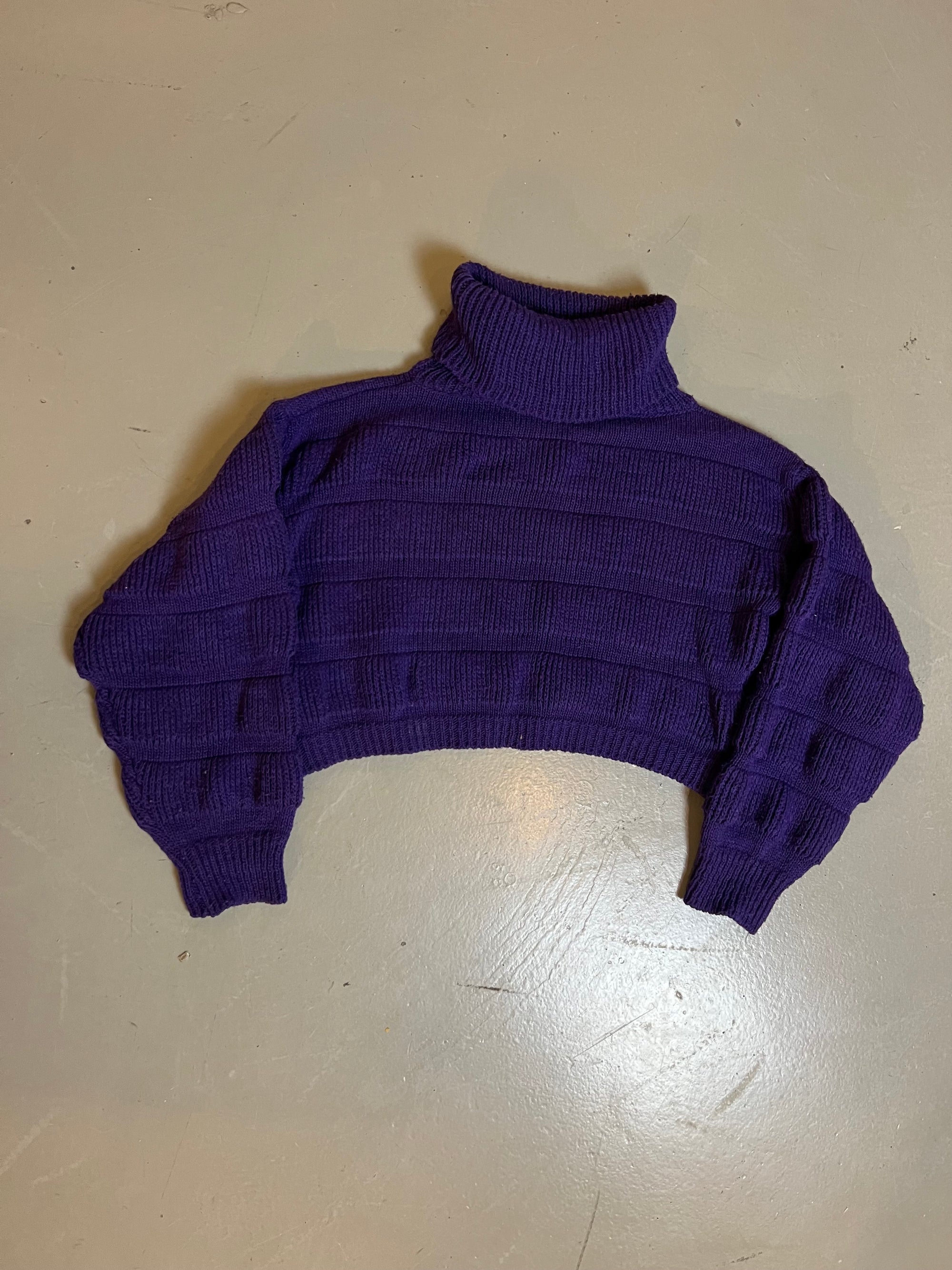 Zu sehen ist ein kurzer lila strickpullover mit Rollkragen 