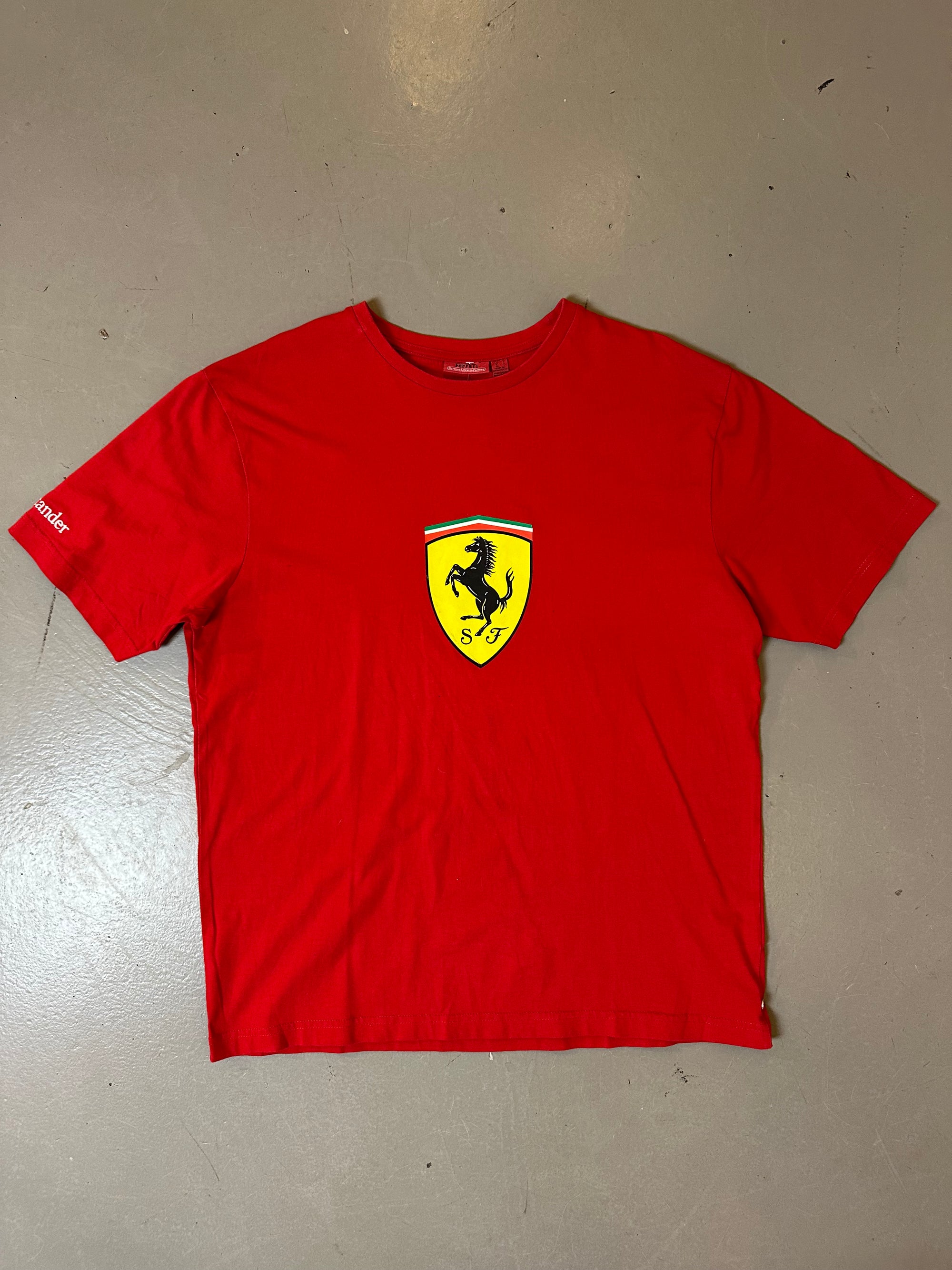 Zu sehnest ein roter Ferrari Tshirt mit dem Logo I der Mitte der Brust 