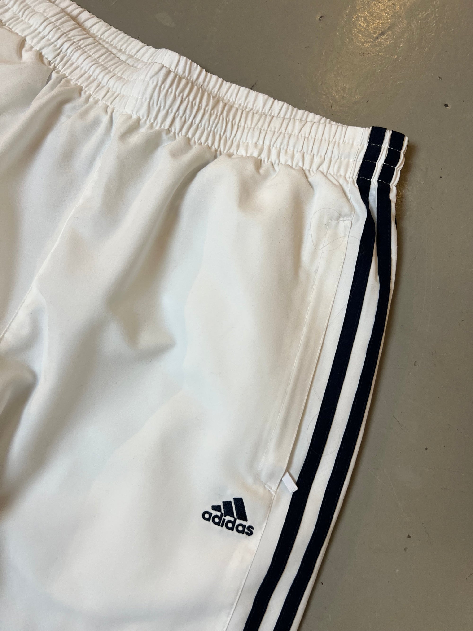 Zu sehen ist eine weiße Adidas Trackpants mit schwarzen Streifen an der Seite 