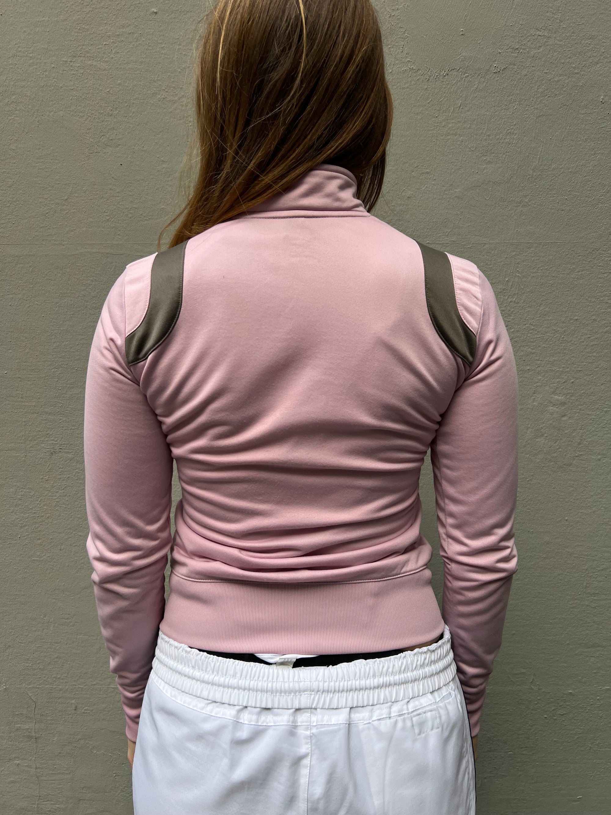 Zu sehen ist eine rosa Nike Trackjacke mit hohem Kragen und braunen Details 