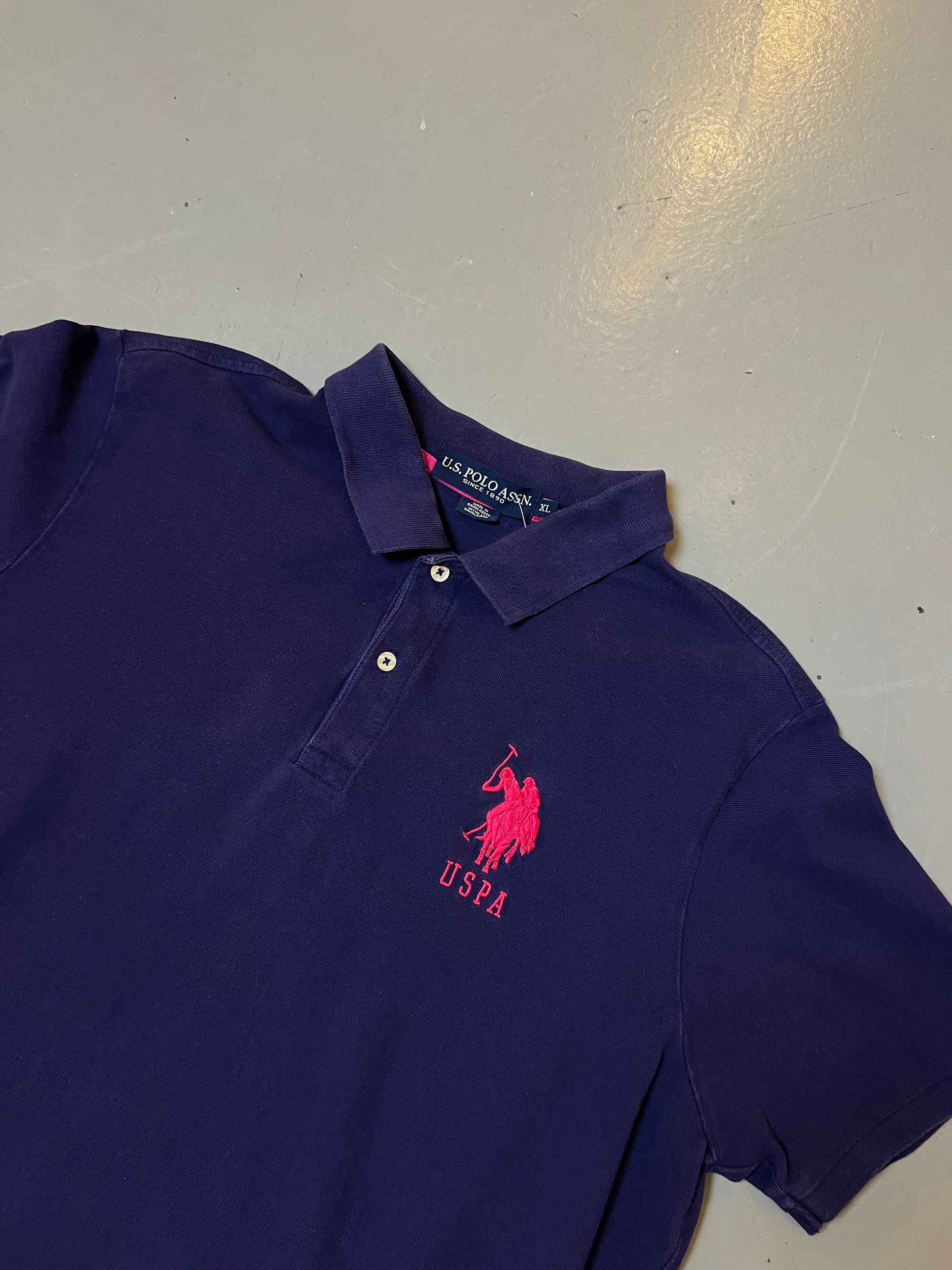 Zu sehen ist Ring lila Polo Shirt von U.S. Polo Assn. mit dem pinken Logo auf der Brust und einer grünen 3 auf dem Ärmel 