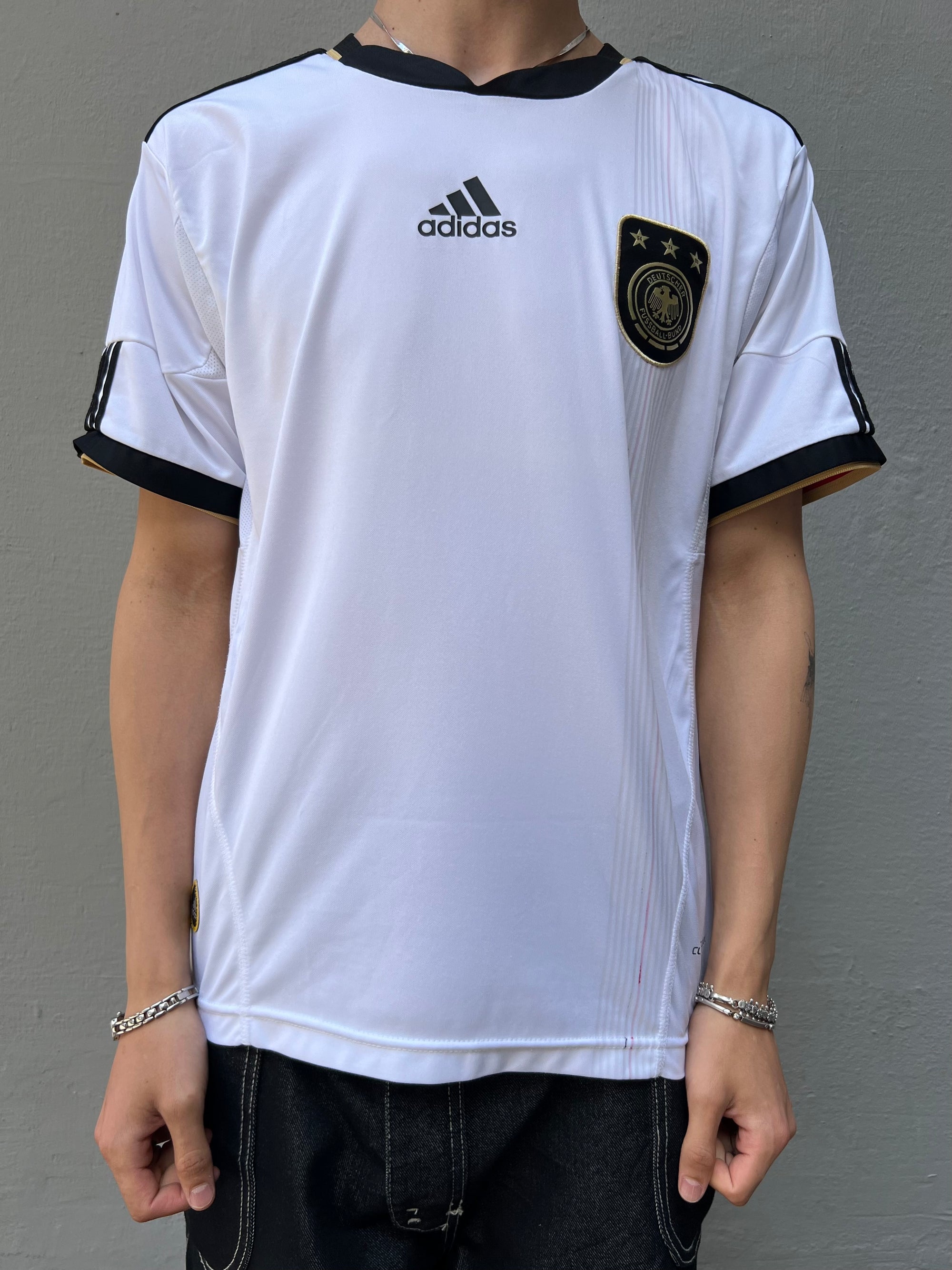 Zu sehen ist ein weißes Vintage Deutschland Trikot getragen vor einem grauen Hintergrund.