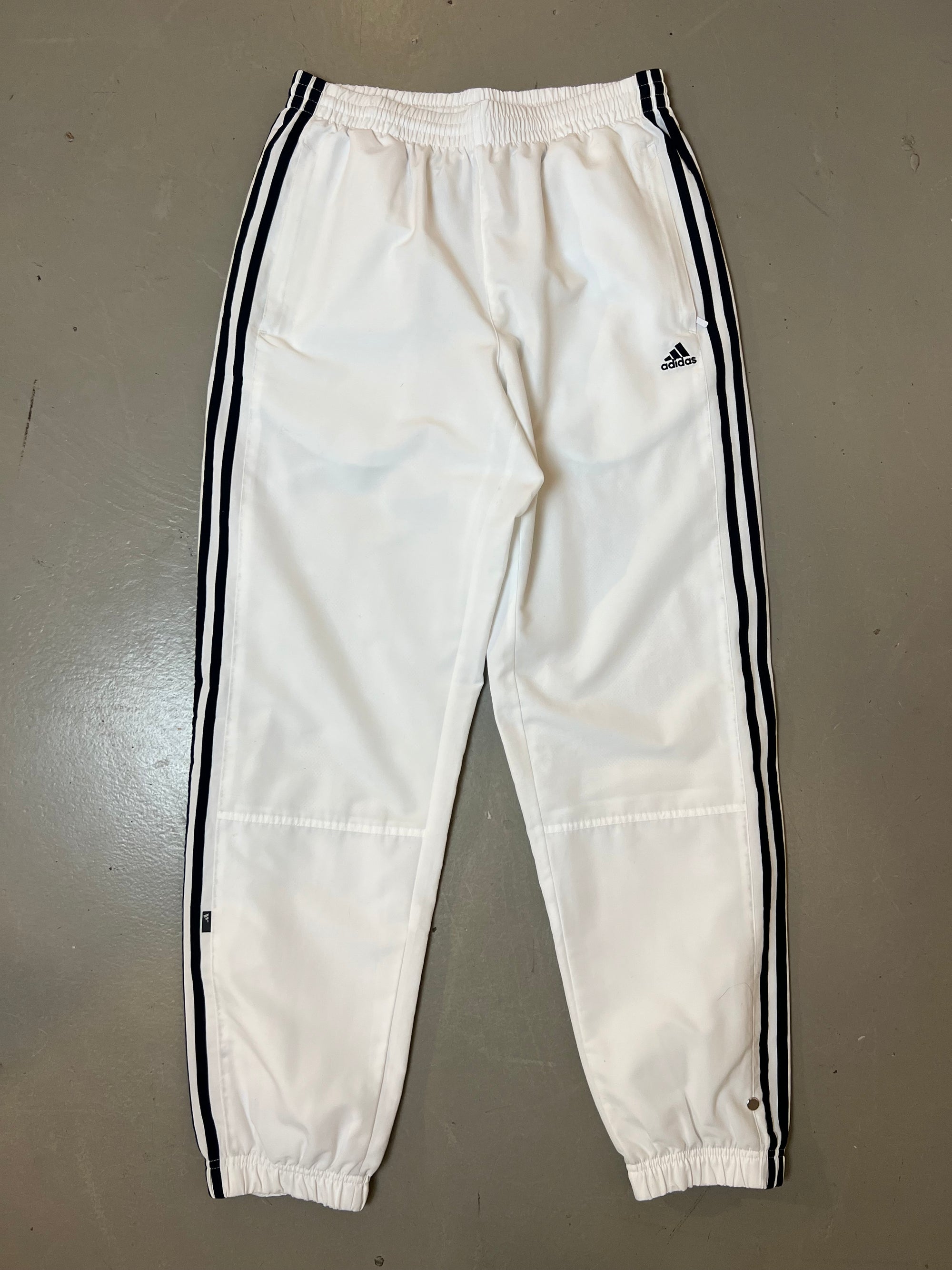 Zu sehen ist eine weiße Adidas Trackpants mit schwarzen Streifen an der Seite 