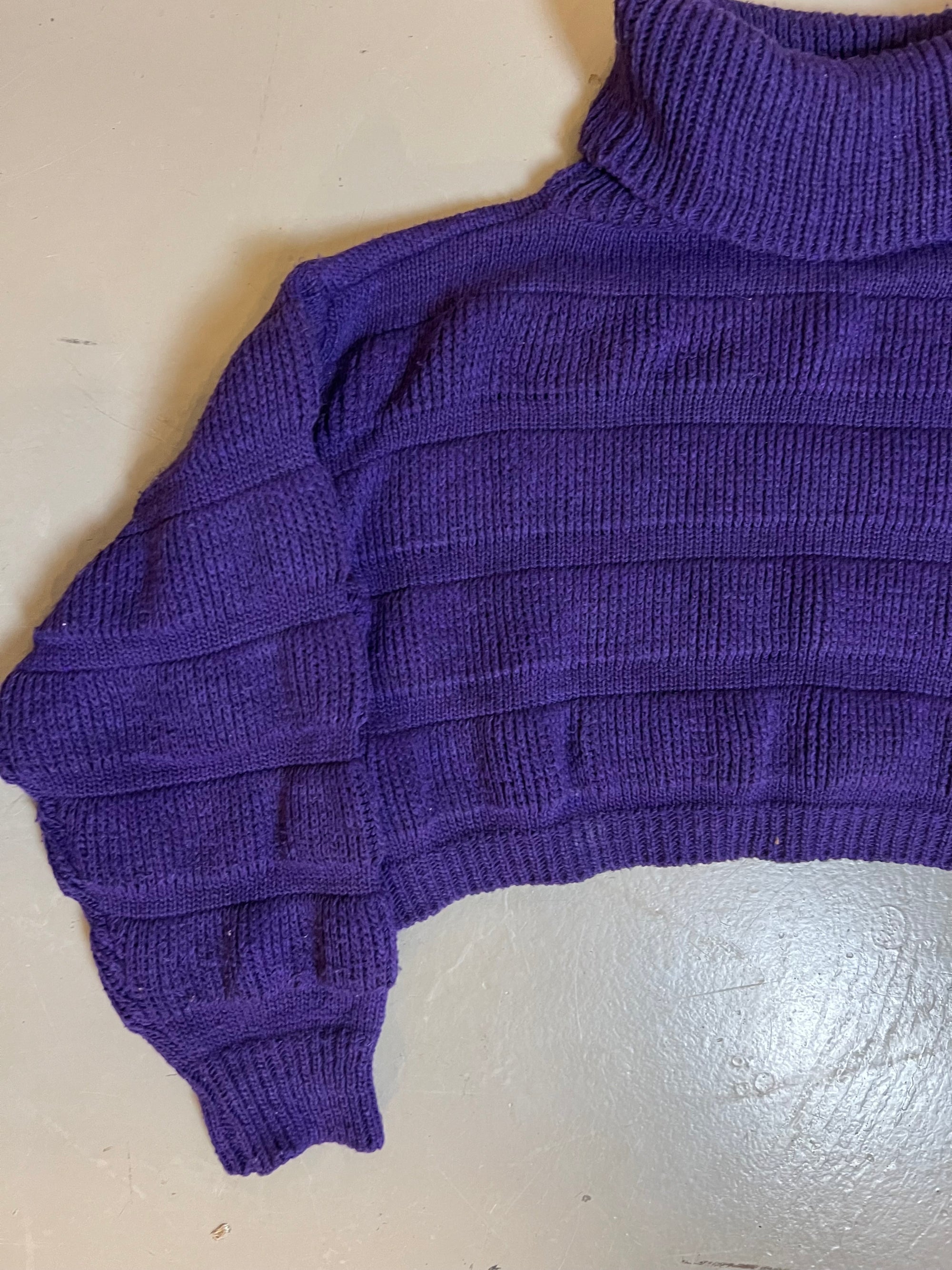 Zu sehen ist ein kurzer lila strickpullover mit Rollkragen 