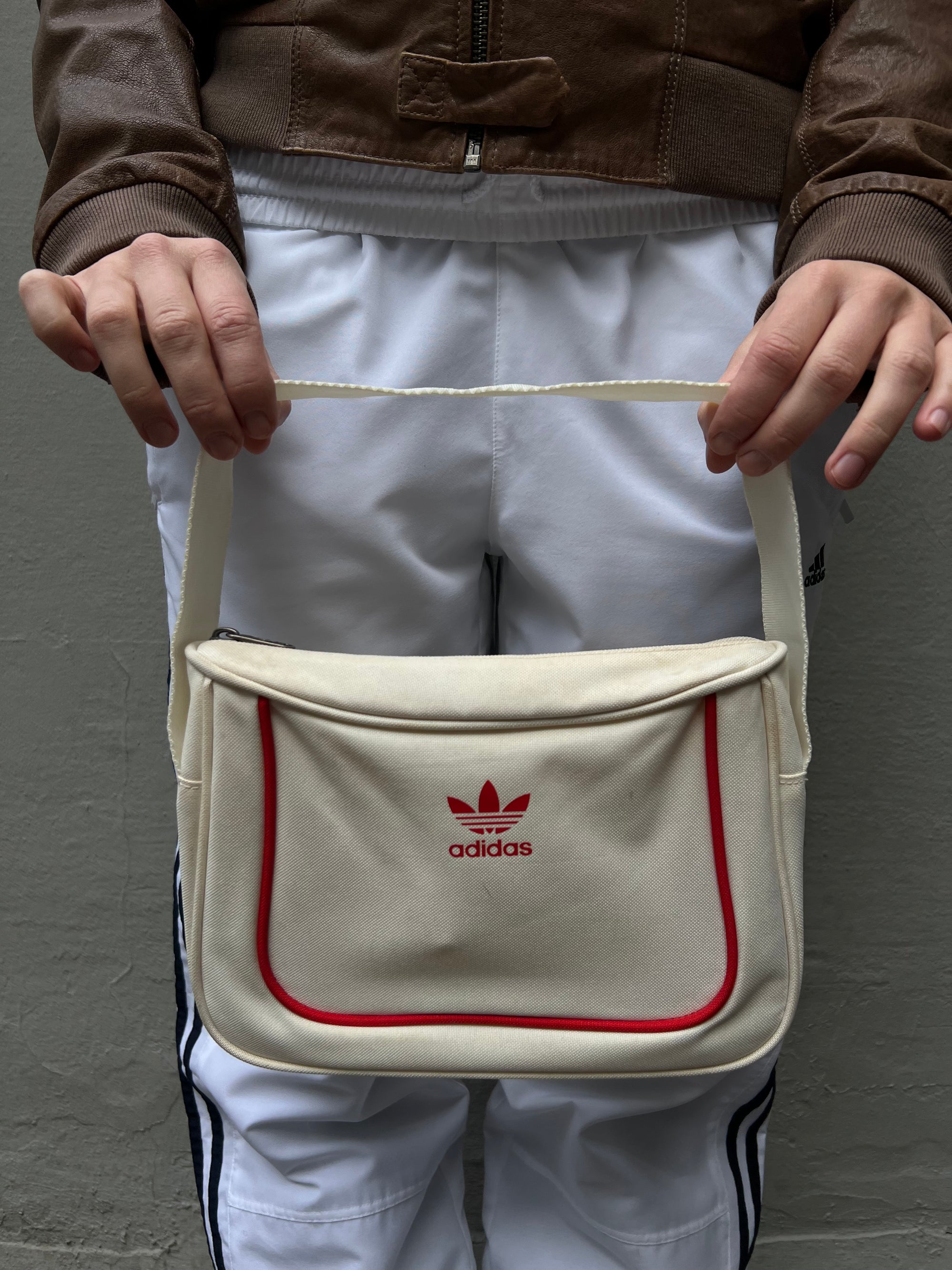 Zu sehen ist eine kleine rechteckige Adidas Tasche in weiß mit roten Details