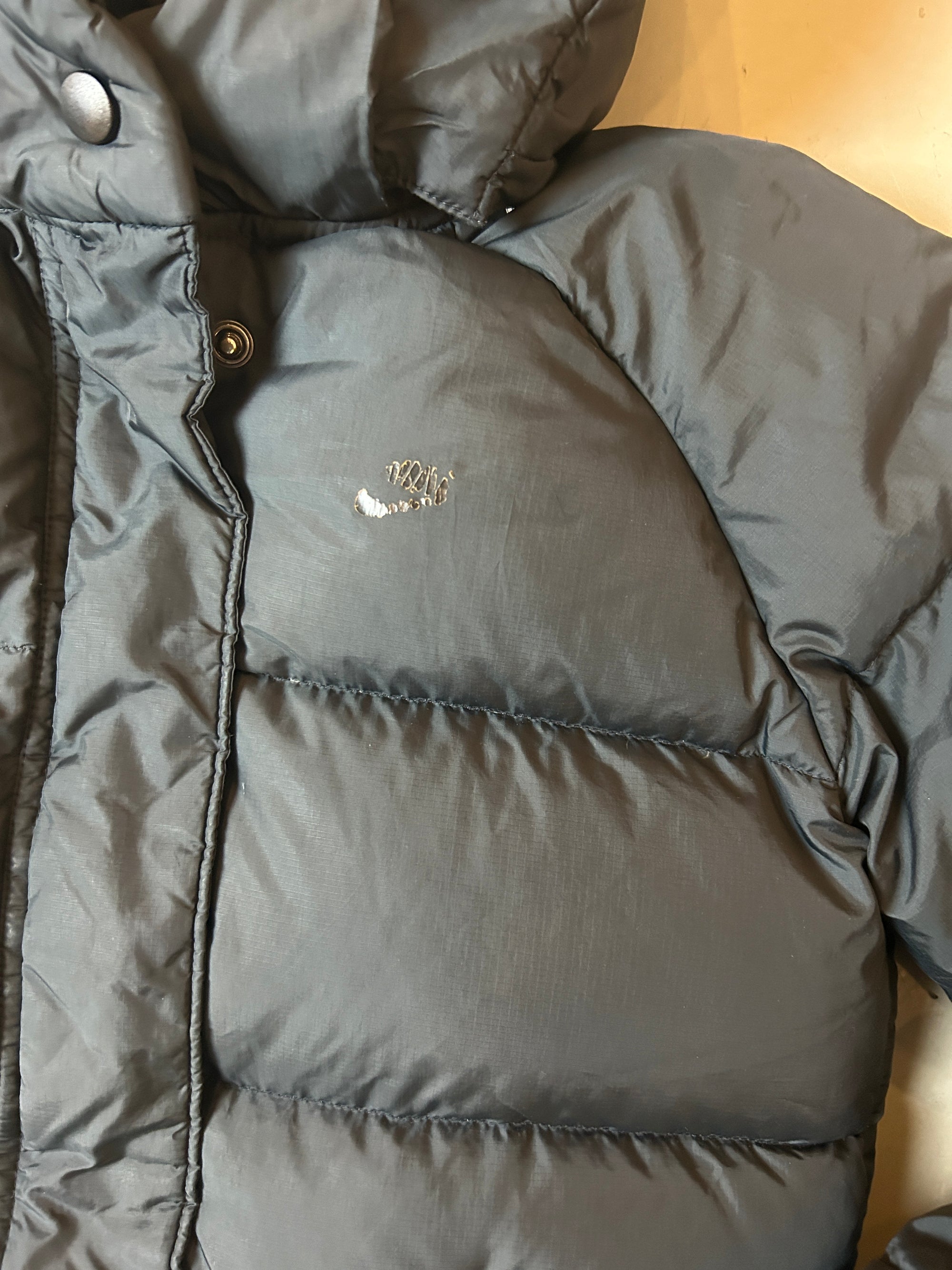 Detailliertes Produktbild von Pufferjacke mit Kapuze von vorne auf grauem Boden 