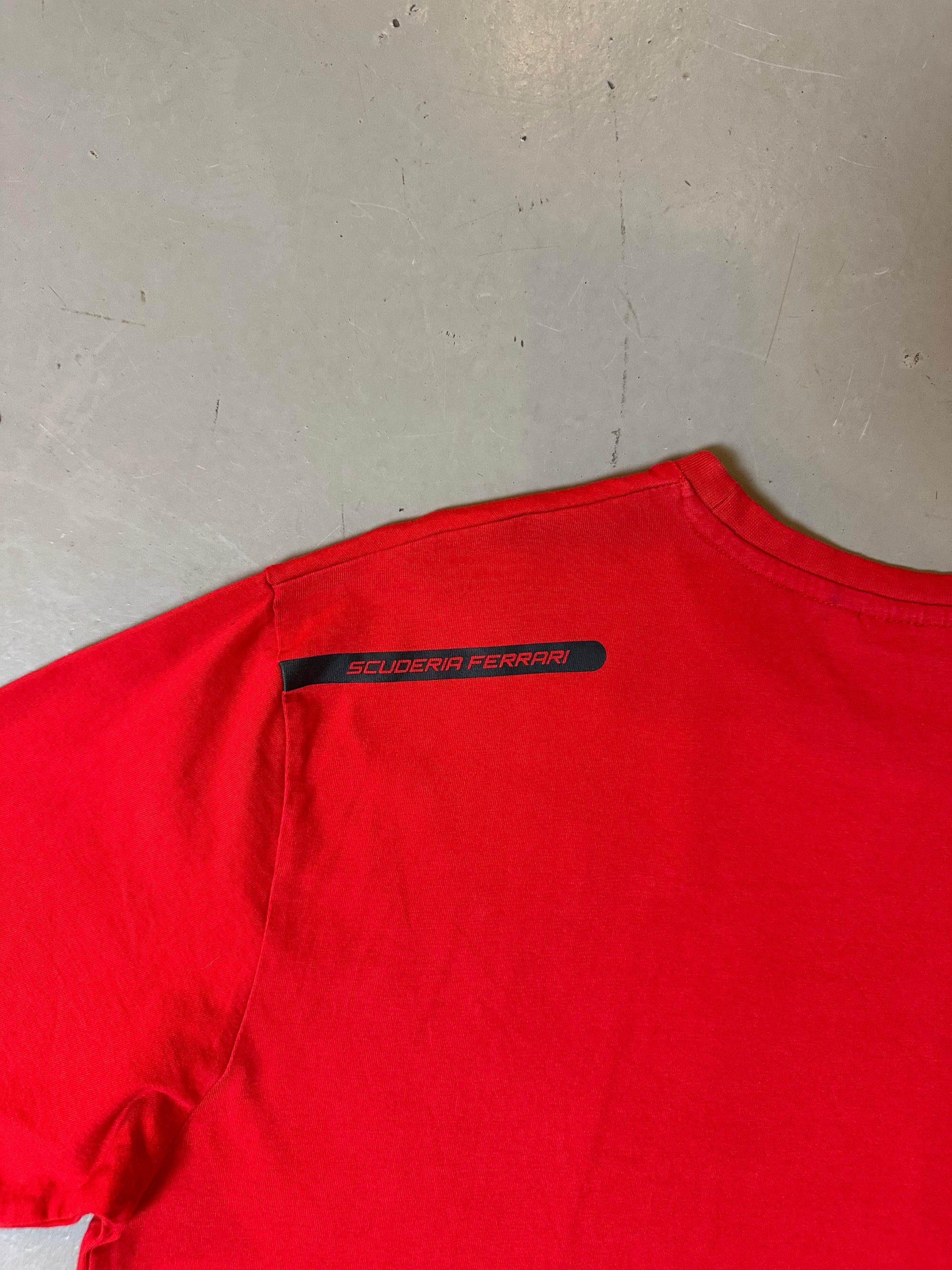 Zu sehnest ein roter Ferrari Tshirt mit dem Logo I der Mitte der Brust 