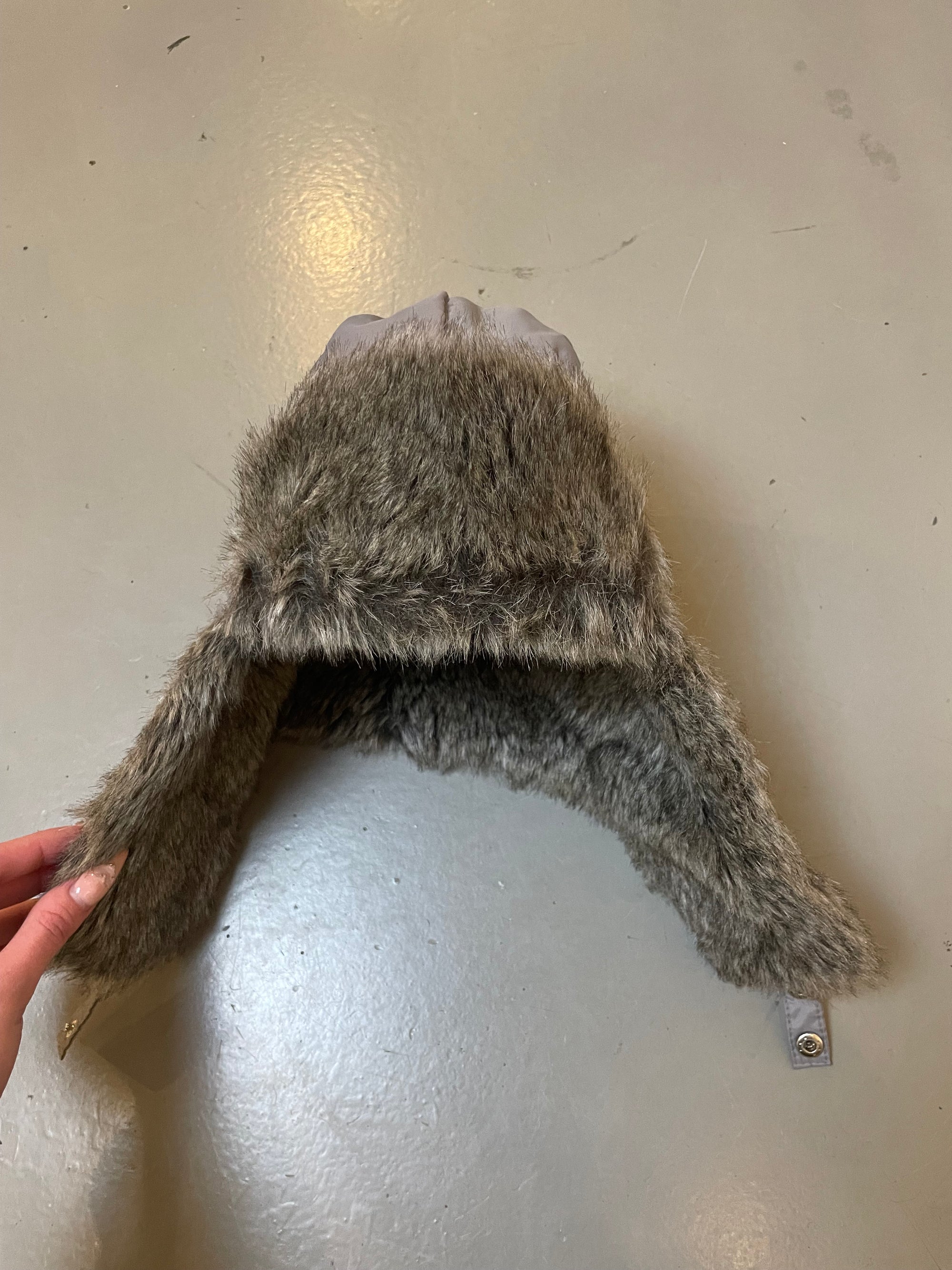 Zu sehen ist eine graue Ushanka mit Fell an der Stirn und den Ohren