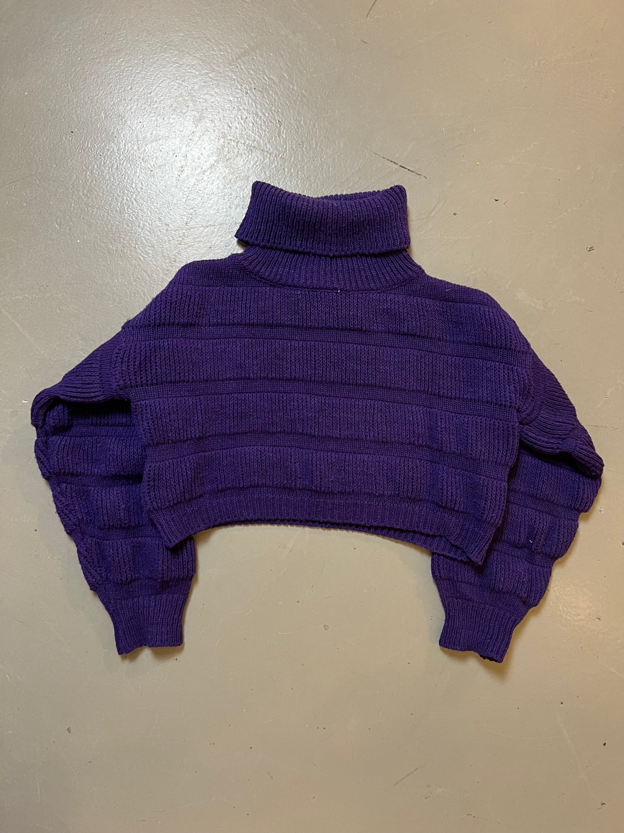 Zu sehen ist ein kurzer lila strickpullover mit Rollkragen 