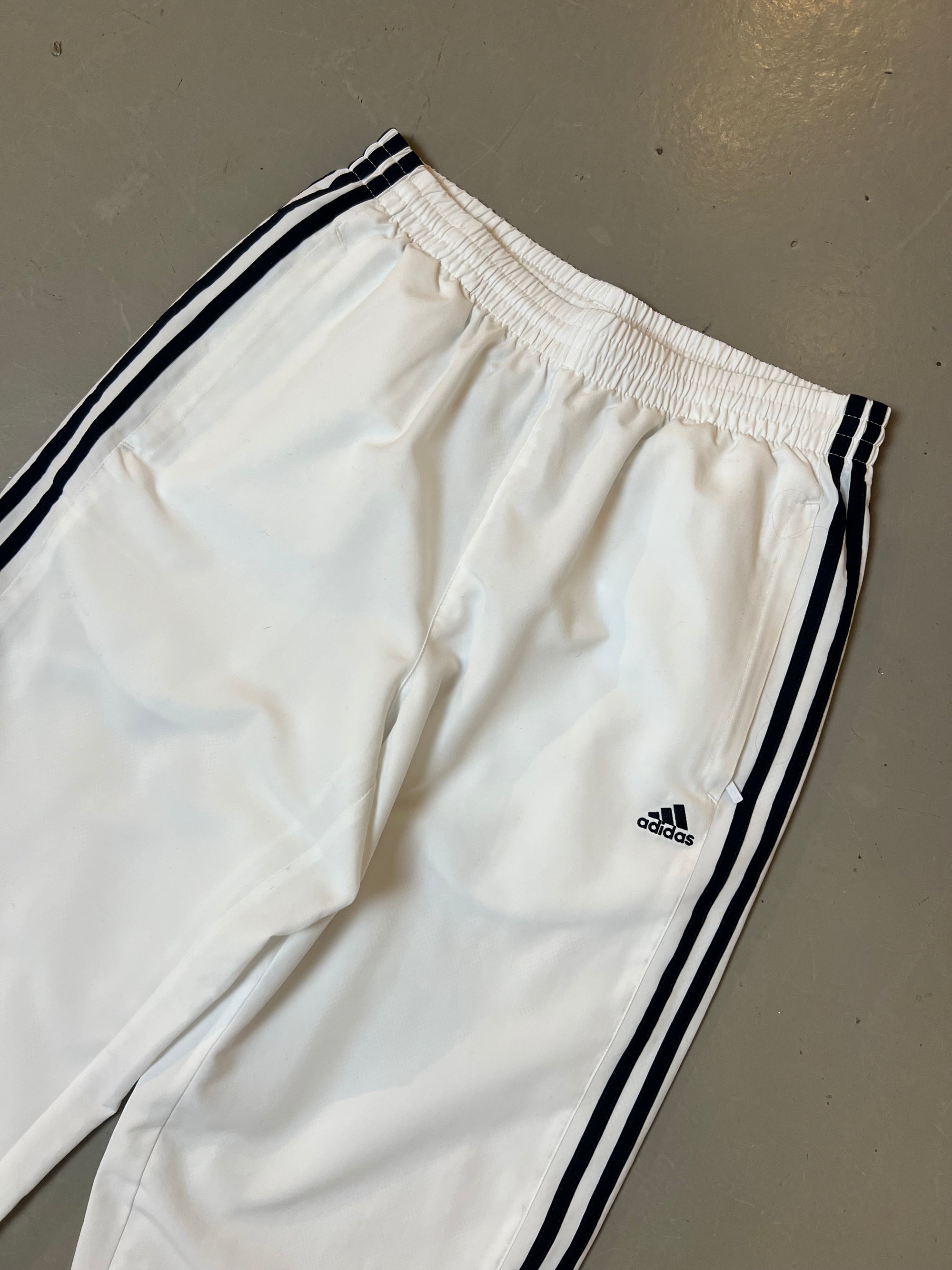 Zu sehen ist eine weiße Adidas Trackpants mit schwarzen Streifen an der Seite 