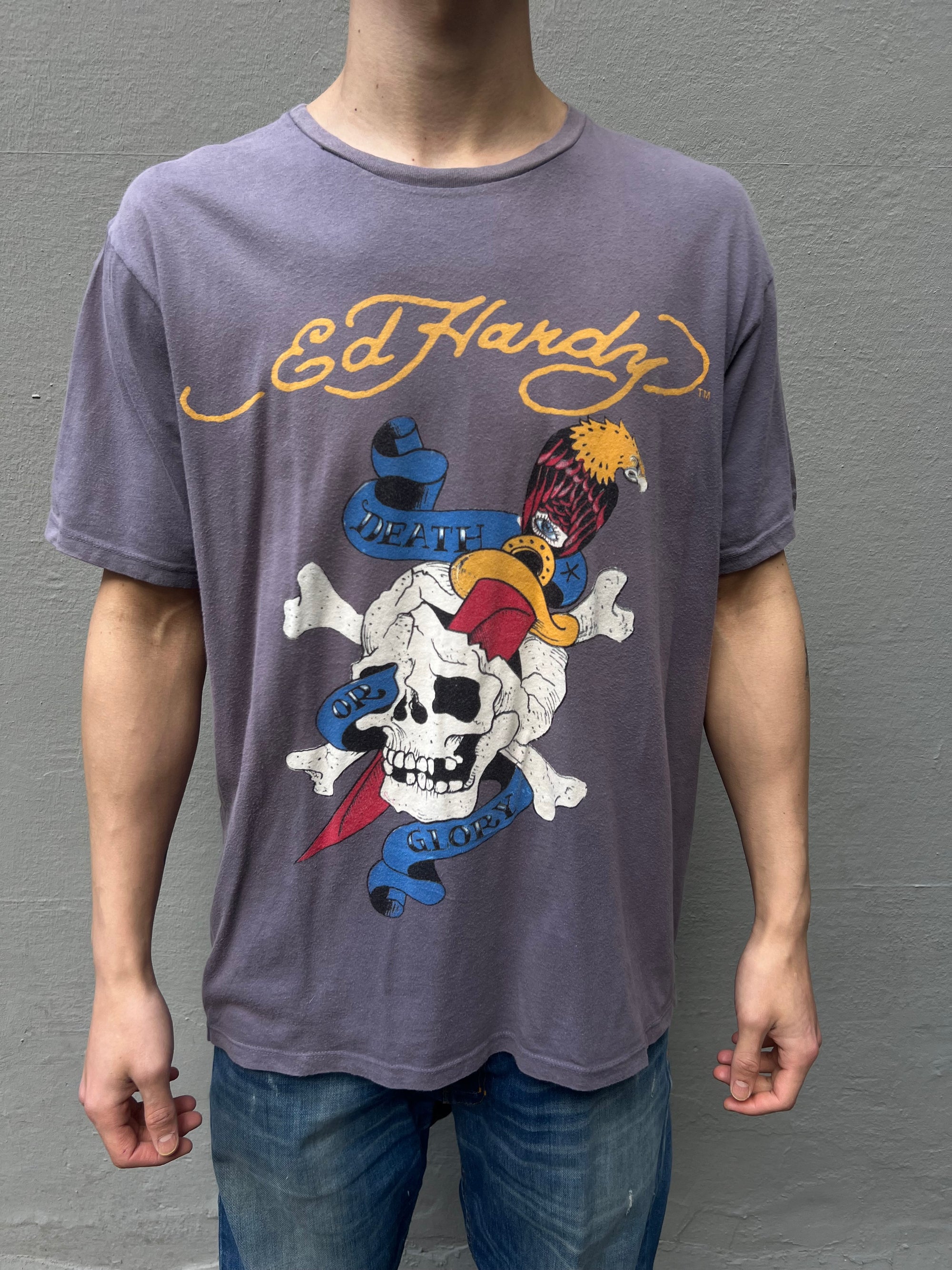 Zu sehen ist ein graues T-Shirt von Ed Hardy mit großem Design auf der Vorderseite und dem Logo auf dem Rücken