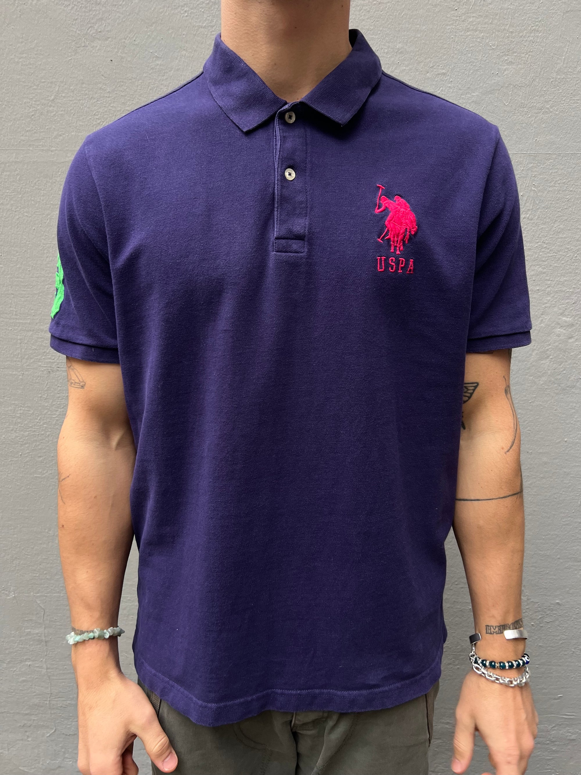 Zu sehen ist Ring lila Polo Shirt von U.S. Polo Assn. mit dem pinken Logo auf der Brust und einer grünen 3 auf dem Ärmel 